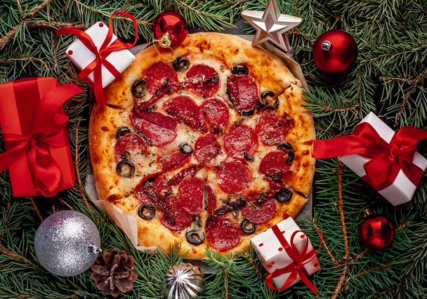 Pizza de Natal com salsichas de salame, mussarela, azeitonas, ervas provençais, molho de tomate, decorado com decorações de Natal, presentes, abeto, brinquedos - Foto, Imagem