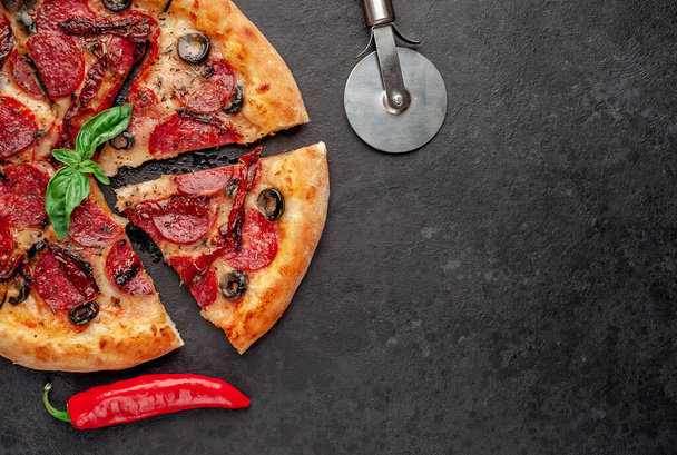 deliciosa pizza de pepperoni en rodajas con salchichas de salami, mozzarella, aceitunas, hierbas provenzales sobre un fondo de piedra - Foto, Imagen
