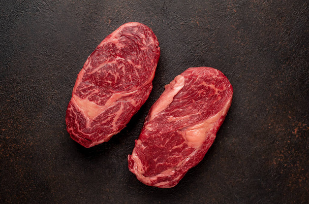 Twee rauwe rundvlees ribeye steaks met specerijen op stenen achtergrond - Foto, afbeelding