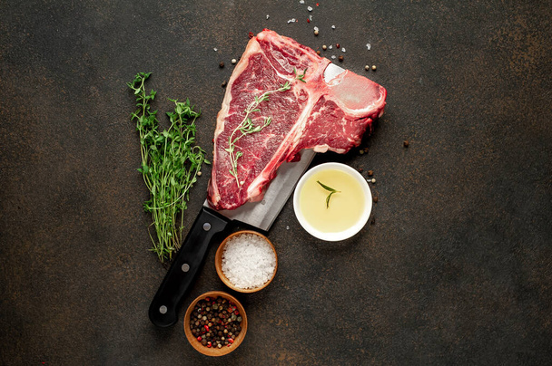 close-up blik van rauwe t-bone steak met ingrediënten op een vleesmes op stenen achtergrond - Foto, afbeelding