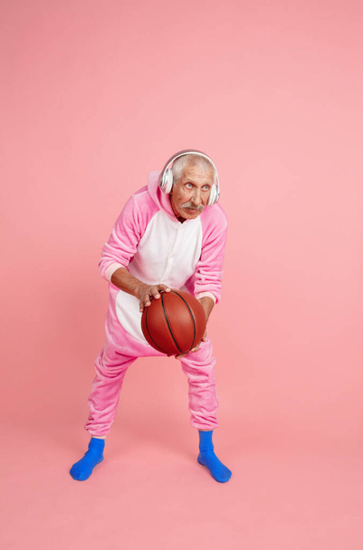 Senior hipster man in stylish pink attire isolated on pink background. Tech and joyful elderly lifestyle concept - 写真・画像