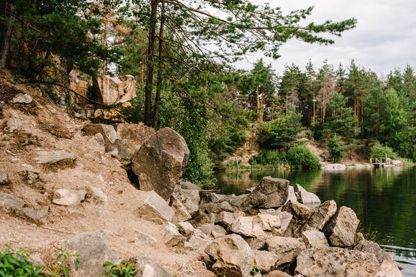 Rocks and stones fall in water. Lake on the background of rocks and fir trees. Canyon. Place for text and design. Landscape of an old flooded industrial granite quarry filled with water. - Photo, image