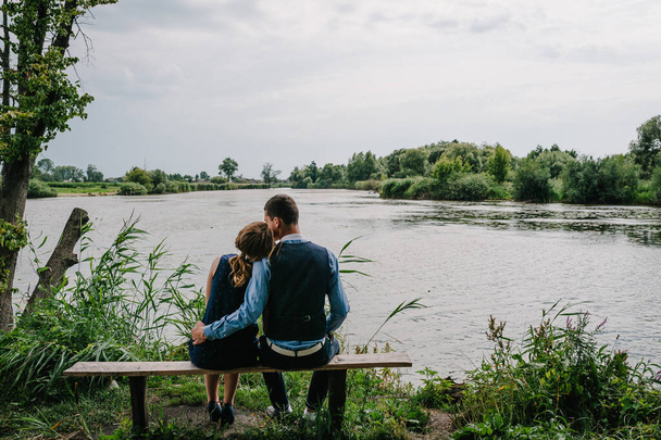 A young couple sitting back on the bench, kissing and hugging  near lake. Nature, landscape. View back. Close up. - Foto, immagini
