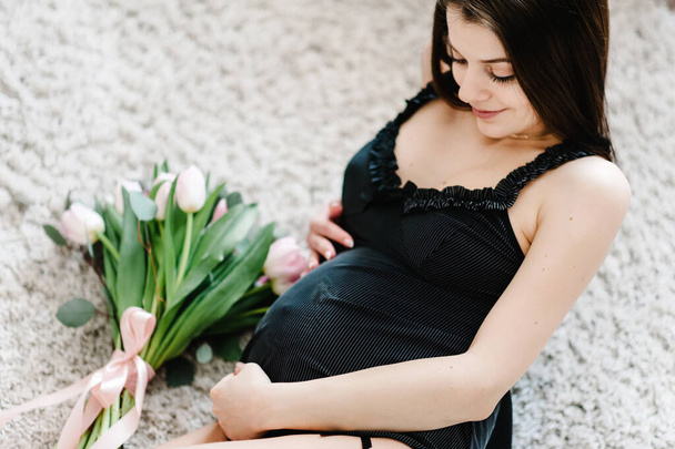 Pregnant happy sexy woman resting and lying on floor or bed, touching her belly holding a bouquet of flowers, hugging tummy at home. Motherhood concept. Pregnancy, expectation. Baby Shower. - Foto, Bild