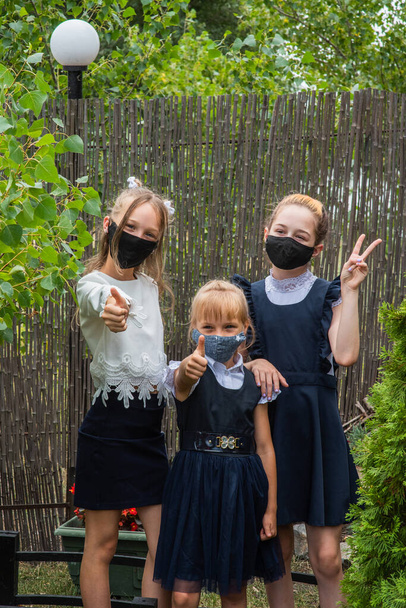 Three schoolgirls wearing masks and going back to school during covid-19 pandemic. Three schoolgirls wearing protective masks. Virus, bacteria, school, protection. Teen girls in school uniform - Photo, Image