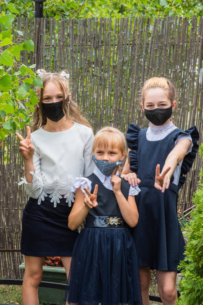Tre studentesse che indossano maschere e tornano a scuola durante la pandemia del Covid-19. Tre studentesse che indossano maschere protettive. Virus, batteri, scuola, protezione. Teen ragazze in uniforme scolastica - Foto, immagini