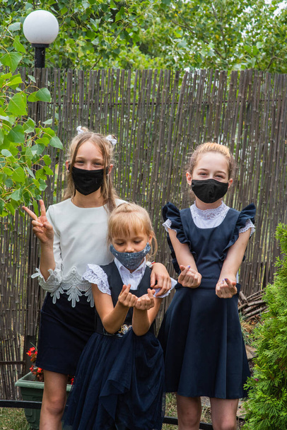 Kolme koulutyttöä naamioituneina ja palaamassa kouluun pandemian aikana. Kolmella koulutytöllä oli suojanaamarit. Virus, bakteeri, koulu, suojelu. Teini tytöt koulupuku - Valokuva, kuva