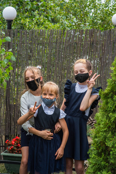 Три школьницы в масках и возвращаются в школу во время пандемии ковид-19. Три школьницы в защитных масках. Вирус, бактерии, школа, защита. Девочки в школьной форме - Фото, изображение