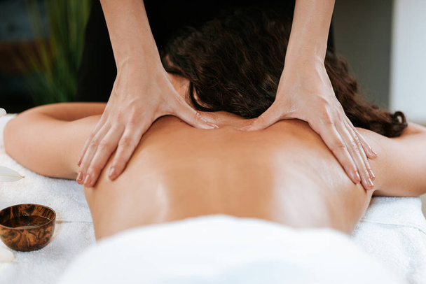 Koncepcja zabiegu kosmetycznego z masażystą i jej pacjentem. Masażysta robi masaż kobiecego ciała w salonie spa. Piękna dziewczyna z brązowymi kręconymi włosami i kreolską skórą o regeneracji masażu. - Zdjęcie, obraz