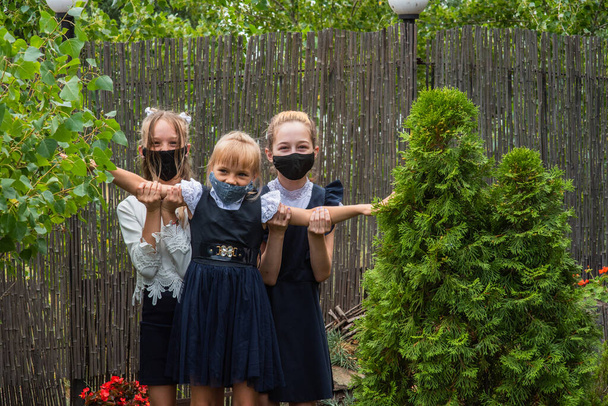 Tres colegialas con máscaras y regresando a la escuela durante la pandemia de covid-19. Tres colegialas con máscaras protectoras. Virus, bacterias, escuela, protección. Chicas adolescentes en uniforme escolar - Foto, imagen