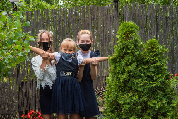 Trois écolières portant des masques et retournant à l'école pendant la pandémie de covidé-19. Trois écolières portant des masques protecteurs. Virus, bactéries, école, protection. Adolescentes en uniforme scolaire - Photo, image