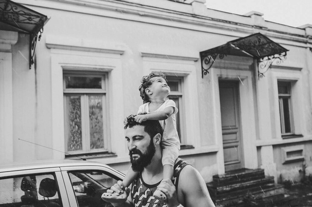 Pai andando com a filha pequena ao ar livre, nas ruas na cidade velha de Tbilisi, na capital da Geórgia, no dia chuvoso de primavera. Pai, rapariga a fugir, à chuva na cidade. Turista. foto preto e branco. - Foto, Imagem