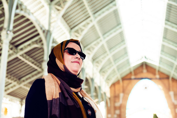 Moslim vrouw met hoofddoek en zonnebril in een gebouw met een metalen dak. kopieerruimte - Foto, afbeelding