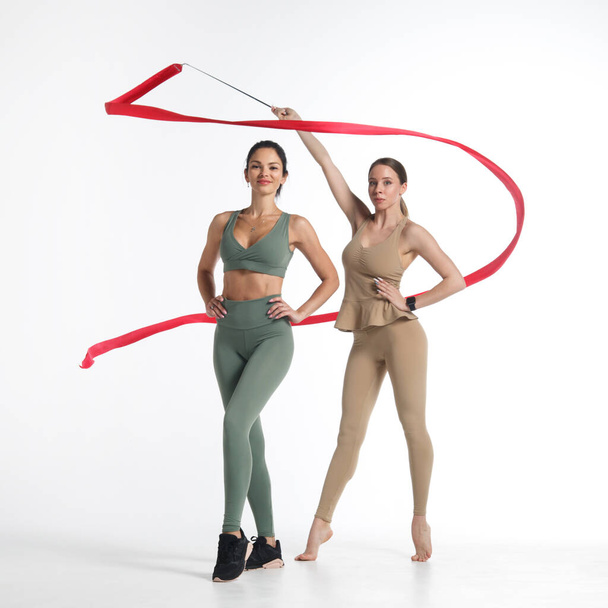Two slim athletic girl perform with red gymnastic ribbon Isolated on a white background. - Φωτογραφία, εικόνα
