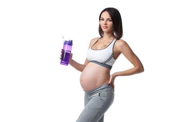 Schlanke athletische Schwangere in Sportbekleidung trinkt Wasser auf weißem Hintergrund. - Foto, Bild