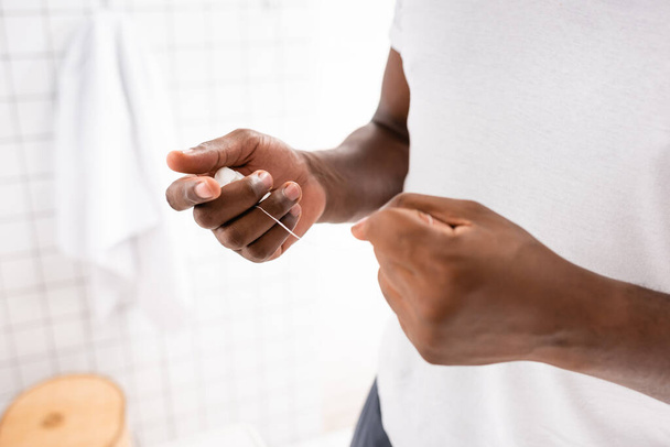 cropped view of afro-american man pulling out dental floss with hands - Фото, зображення