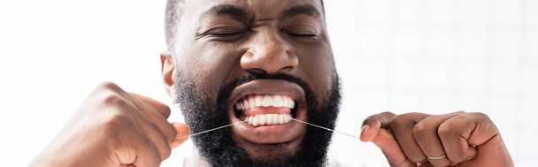 plano panorámico del hombre afroamericano con los ojos cerrados usando hilo dental - Foto, imagen