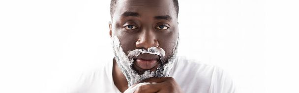 plano panorámico de hombre afroamericano con espuma de afeitar en la cara mirando a la cámara - Foto, Imagen