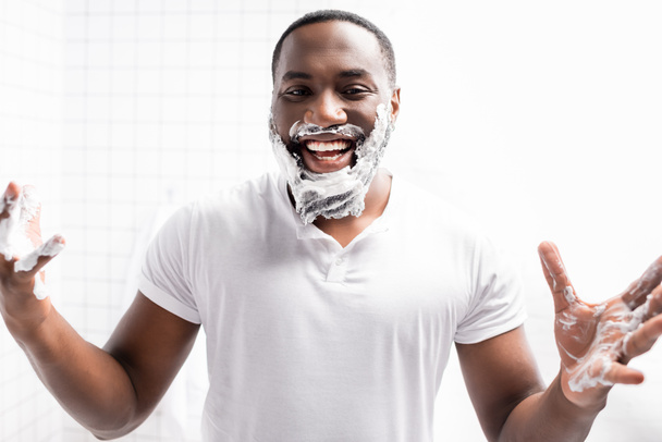 smějící se afro-americký muž s pěnou na holení na obličeji při pohledu do kamery - Fotografie, Obrázek
