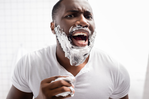 hombre afroamericano aplicando espuma de afeitar con boca abierta - Foto, imagen