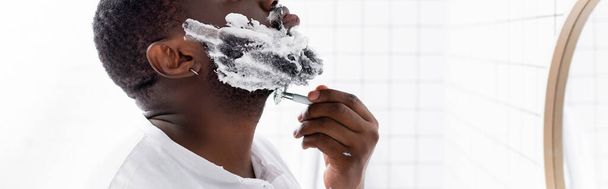 plano panorámico de hombre afroamericano afeitando barba con navaja de afeitar  - Foto, imagen