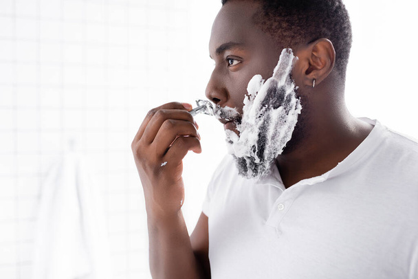Afroamerikanischer Mann rasiert Bart mit Rasiermesser  - Foto, Bild