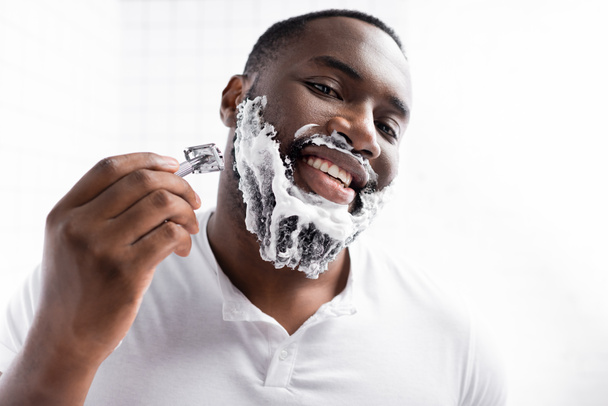 portrait of happy afro-american man shaving beard with razor  - Foto, imagen