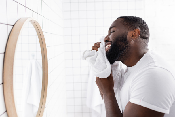 sonriente afroamericano hombre secando barba con toalla  - Foto, imagen