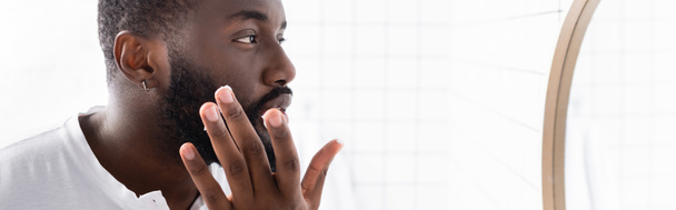 plano panorámico del hombre afroamericano aplicando cura para fortalecer el crecimiento de la barba - Foto, Imagen