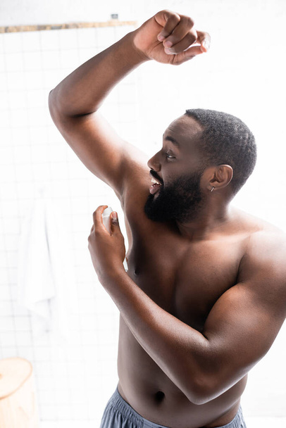 smiling afro-american man with hand up using deodorant - Foto, Bild