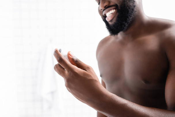 vista recortada de hombre afroamericano sonriente sosteniendo desodorante en la mano - Foto, Imagen