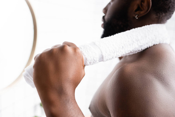 partial view of serious afro-american man looking in mirror with towel behind neck  - Foto, immagini