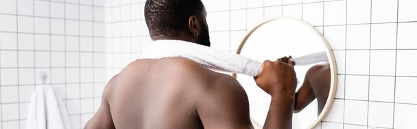 Panoramaaufnahme eines afroamerikanischen Mannes, der mit einem Handtuch im Nacken in den Spiegel blickt  - Foto, Bild