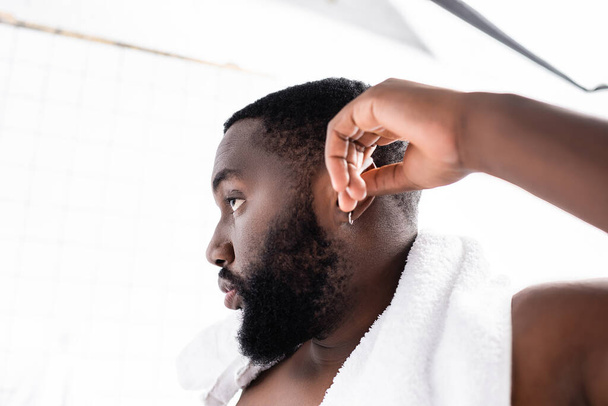 vista lateral de hombre afro-americano limpiando orejas con palo de oreja - Foto, imagen