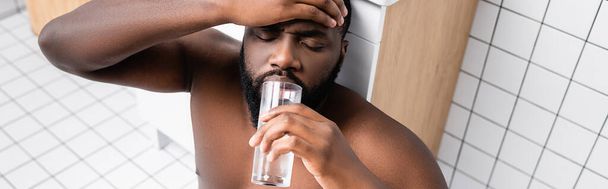 tiro panorâmico do homem afro-americano que sofre de ressaca e água potável - Foto, Imagem