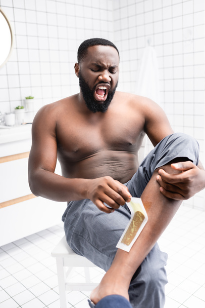 afro-american man tearing off wax strips and screaming from pain  - Photo, Image