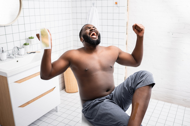 hombre afroamericano arrancando tiras de cera y gritando de dolor  - Foto, Imagen