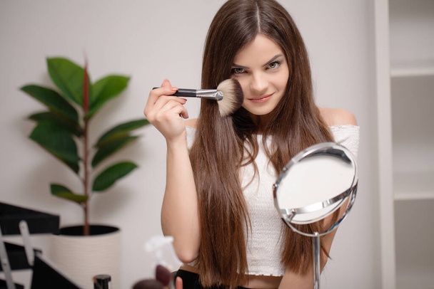 Молодая женщина наносит макияж на лицо дома - Фото, изображение