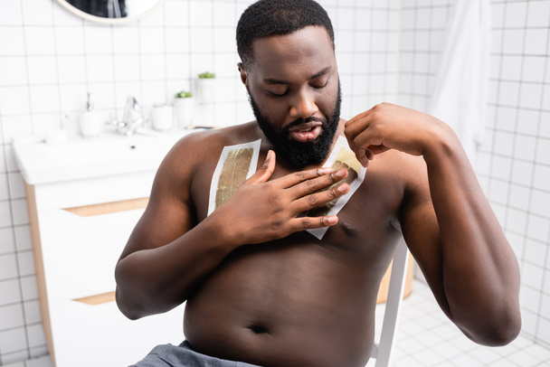 Afrikaans-Amerikaanse man die wax strips op de borst aanbrengt  - Foto, afbeelding