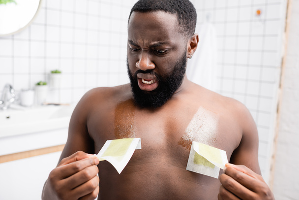 geschokt afro-Amerikaanse man scheuren van wax strips  - Foto, afbeelding