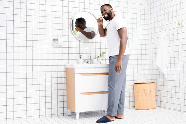 full length of afro-american man brushing teeth and looking back - Foto, afbeelding