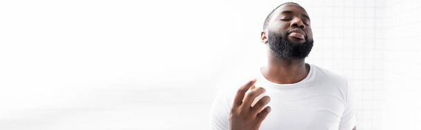 plano panorámico del hombre afroamericano en camiseta blanca usando perfume - Foto, imagen