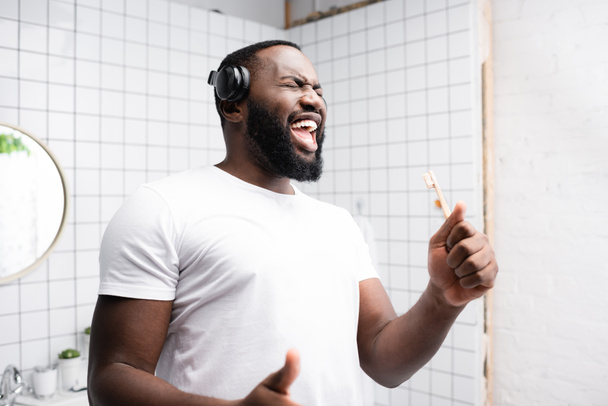afro-american man with headphones singing in toothbrush - Foto, Bild