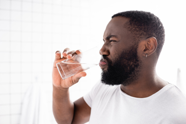 hombre afroamericano haciendo muecas y bebiendo agua - Foto, imagen
