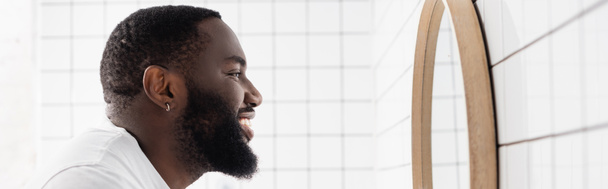 panoramatický záběr afro-amerického muže usmívajícího se a dívajícího se do zrcadla - Fotografie, Obrázek