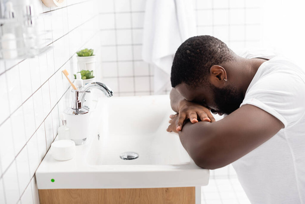 hombre afro-americano cansado apoyado cabeza en el fregadero  - Foto, imagen