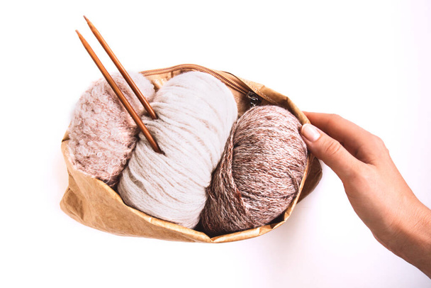 Woman's hand holds a craft eco bag with skeins of yarn in nude colors and knitting needles on a white background. Copy space. Knitwear as a concept of female hobby. Front view - Valokuva, kuva