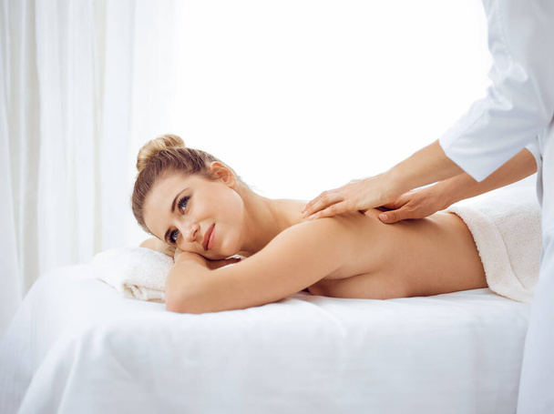Young and blonde woman enjoying massage of back in spa salon. Beauty concept - Foto, Imagem