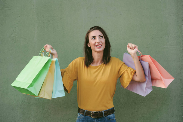 sonriente mujer joven sosteniendo una bolsa de compras sobre fondo verde - Foto, imagen