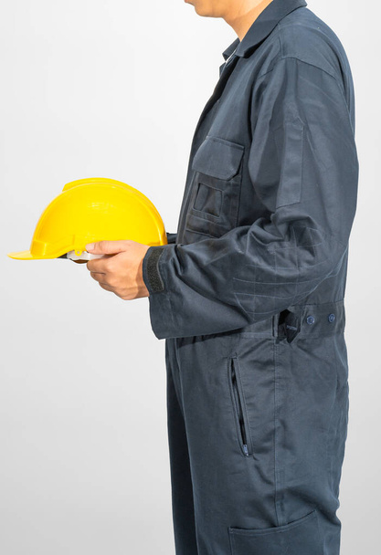 Работник, стоящий в синем комбинезоне с жёлтой каской на сером фоне - Фото, изображение